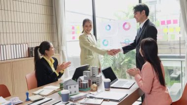 Emlak işadamı müşteriyle tokalaşıyor, satış kapanıyor, danışmanlık yapıyor ve masa başında konuşuyor, imzalamadan önce sözleşmeyi tartışıyor, el sıkışıyor, yavaş çekim videosu çekiyor..