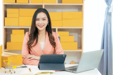 Genç Asyalı kadın evde dizüstü bilgisayar ve paket kutusuyla çalışıyor. Online alışveriş ve teslimat konsepti. KME işi.