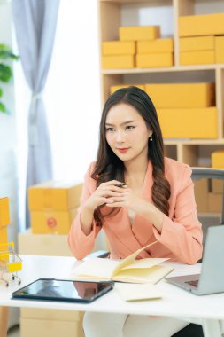 Genç Asyalı kadın evde dizüstü bilgisayar ve paket kutusuyla çalışıyor. Online alışveriş ve teslimat konsepti. KME işi.