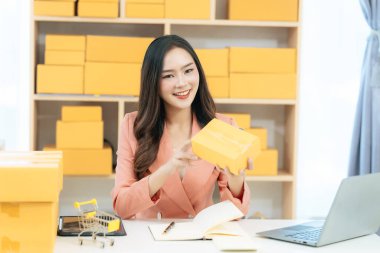 Genç Asyalı kadın evde dizüstü bilgisayar ve paket kutusuyla çalışıyor. Online alışveriş ve teslimat konsepti. KME işi.