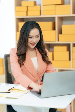 Genç Asyalı kadın evde dizüstü bilgisayar ve paket kutusuyla çalışıyor. Online alışveriş ve teslimat konsepti. KME işi.