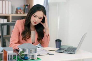 Asyalı stresli bir emlakçı kadın ofis masasında çalışıyor..