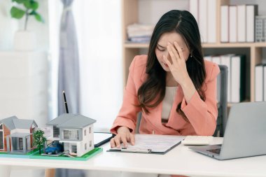 Asyalı stresli bir emlakçı kadın ofis masasında çalışıyor..