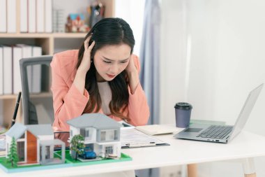 Asyalı stresli bir emlakçı kadın ofis masasında çalışıyor..