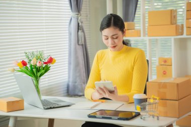 Portrait of young Asian woman using mobile phone, online shopping concept for SME entrepreneurs or freelancers, young small business entrepreneurs working with smartphone at home.