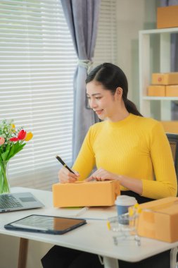 Cheerful Asian small business owner working in office with online sales and package delivery in home office.