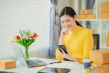 Portrait of young Asian woman using mobile phone, online shopping concept for SME entrepreneurs or freelancers, young small business entrepreneurs working with smartphone at home.