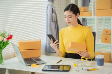 Portrait of young Asian woman using mobile phone, online shopping concept for SME entrepreneurs or freelancers, young small business entrepreneurs working with smartphone at home.