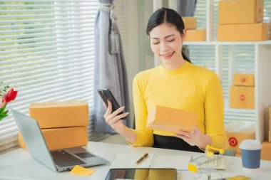 Portrait of young Asian woman using mobile phone, online shopping concept for SME entrepreneurs or freelancers, young small business entrepreneurs working with smartphone at home.