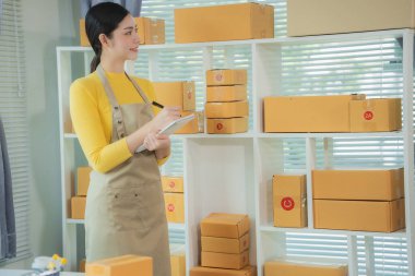 Cheerful Asian small business owner working in office with online sales and package delivery in home office.