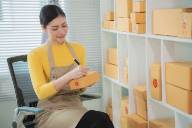 Cheerful Asian small business owner working in office with online sales and package delivery in home office.