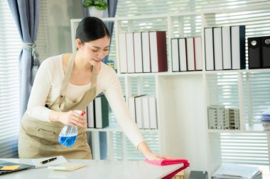 Asian female cleaner uses cloth and sprays disinfectant to wipe glass table cleaner house