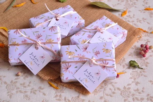 stock image Making small gifts for wedding guests handmade soaps wrapped in floral watercolor pattern paper in natural pastel colors and decorated with pink ribbon and labels, creative bridal ideas, handmade artisan favors, beautiful packaging