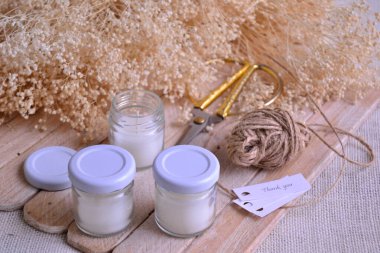 Düğün mumları küçük ev işleri yapar, çevrimiçi zanaatkar el yapımı ürünler satar, orijinal olay hatıra eşyaları, hediye olarak ev yapımı ürünler, beyaz cam kavanoz mumları tahta jüf kurdele arka planı, pahalı zanaat etkinliği.