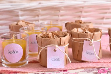 Vaftiz kız bebek partisi, camda balmumu mumlar, el yapımı ambalaj kağıdı, pamuk kurdele ve pembe etiketli bebek ismi, beyaz hasır ve jüt arka plan, orijinal parti hatırası.