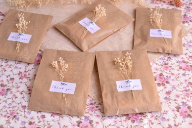 Düğün kutuları içinde özel etiketli paketler ve kuru çiçek süslemeleri, ekolojik parti hediyeleri doğal renklerde.