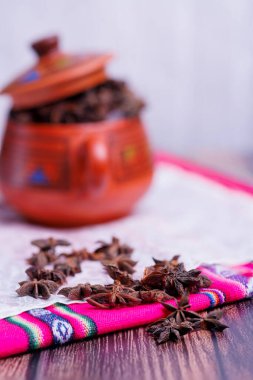 Eski ahşap bir masa üzerinde yıldız anason içeren kil kavanozu ve Peru dağlarından bir masa örtüsü.