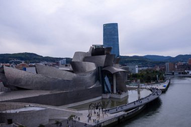 Bilbao, İspanya, 12 Temmuz 2024 - Bilbao 'daki Guggenheim Müzesi açık gün ışığında görkemli bir şekilde nehir kıyısında duruyor, titanyum yüzeyi güneşin altında parlıyor. Frank Gehry 'nin yenilikçi mimarisi tamamen sergilenmektedir.