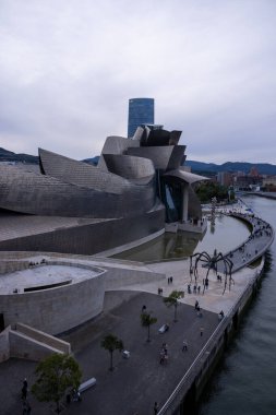 Bilbao, İspanya, 12 Temmuz 2024 - Gündüz vakti, Bilbao 'daki Guggenheim Müzesi nehir kenarındaki ortamı ile uyumlu hale gelir. Titanyum perade güneş ışığını yansıtıyor, binanın sıvı formlarını ve yenilikçi tasarımını geliştiriyor. Açık gökyüzü ve sükunet