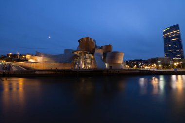 Bilbao, İspanya, 12 Temmuz 2024 - Bilbao 'daki Guggenheim Müzesi geceleri göz kamaştırıcı bir şekilde parlıyor. Sakin nehirdeki yansımalar ve müzenin cesur tasarım unsurları büyüleyici bir gece yaratıyor.