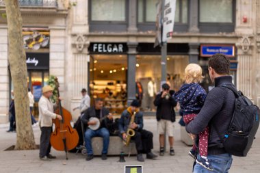 Barselona, İspanya, 31 Ekim 2023 - Bu canlı akşamda, La Rambla bir baba olarak açık hava konser salonuna dönüşür ve genç kızı spontane bir müzik performansı paylaşır. Kalabalık kalabalığın ve hareketli sokak hayatının ortasında