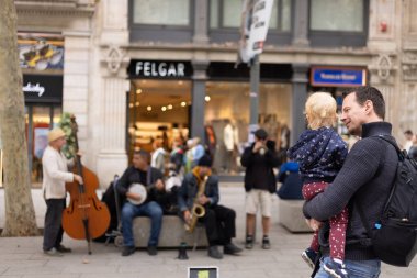 Barselona, İspanya, 31 Ekim 2023 - Çocuğunu kollarında tutan bir baba, her ikisi de bir sokak konserinin melodileri ile büyülenmişti..