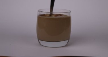 Taze demlenmiş kahveyle dolu kristal bir bardak, şekerle yavaşça karıştırılan bir kaşık. Yavaş çekim etkisi, beyaz arka planda çözünen şekeri vurgular