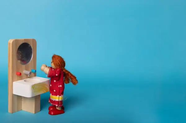 stock image A wooden toy of a redheaded girl with braids washing her face, set against a blue background. Charming and playful