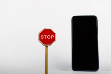 Beyaz arka planda, ahşap bir oyuncak dur tabelası akıllı telefonun yanında duruyor. Bu kavramsal fotoğraf farklı iletişim türleri arasındaki etkileşimi vurgular