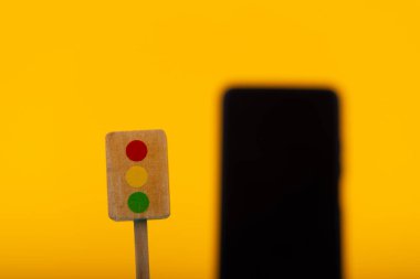 Arka planda bulanık bir akıllı telefonla, teknoloji ve oyun arasındaki kavramsal zıtlığı vurgulayan ahşap bir oyuncak trafik ışığı sarı bir arka plana odaklanmış durumda.