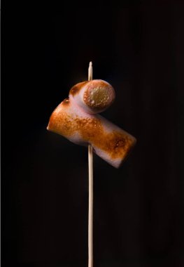 Marshmallows turn golden-brown and melt under a torch's heat. The black background provides a striking contrast to the process, making it visually appealing.