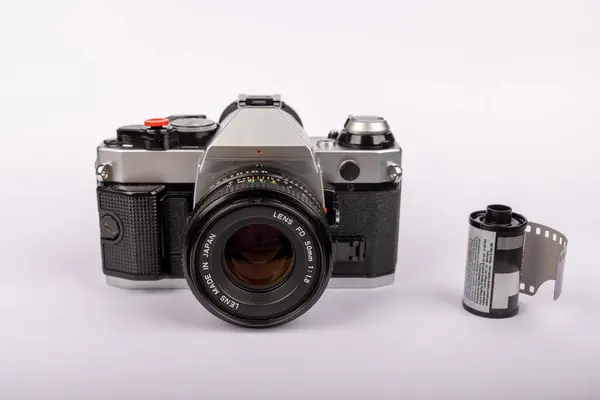 stock image Antique camera positioned in the middle of a white backdrop, with several 35mm film rolls arranged around it. Evokes a classic photographic era.