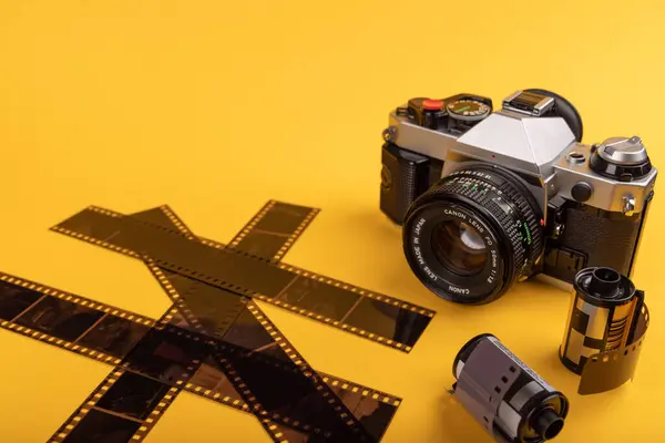 stock image A vintage camera and developed 35mm film rolls take center stage against a yellow background, evoking memories of the golden age of film photography.