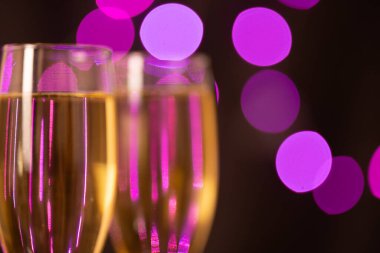 Şampanyayla dolu zarif şampanya kadehleri, sol tarafta siyah arka planda, bulanık menekşe ışıklarıyla dizilmiş, yeni yıl arifesi kutlamaları için mükemmel..