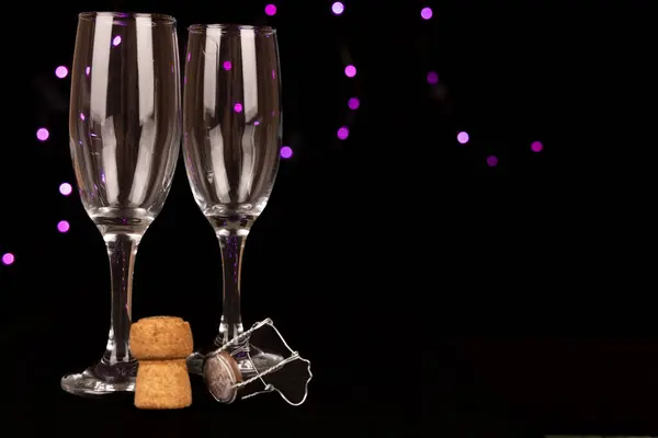 Stock image Detailed view of empty champagne glasses, a cork, and a bottle against a black backdrop with violet bokeh lights. Perfect for celebrating New Year's Eve.