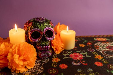 A skull decorated with metallic flowers, placed between two lit candles. Orange flowers and more candles are carefully arranged for the celebration