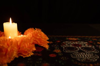 Resmin sol tarafında canlı turuncu kadife çiçekleriyle çevrili üç mum var. Siyah bir arkaplan karşısında, sahne sadece mum ışığıyla aydınlatılır, bir Dia de los Muertos masa örtüsüyle..