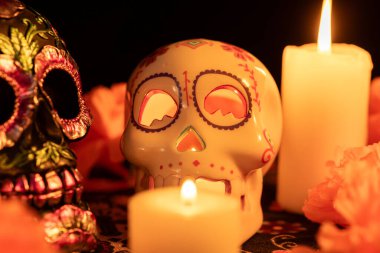 Siyah bir fonda iki zıt kafatası bulunur: biri metalik çiçeklerle süslenmiş, diğeri ise yanan bir mum tutmaktadır. Kadife çiçekleri ve mumlar Ölüm Günü 'nde şenlikli bir dokunuş ekler..