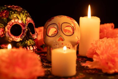 Metal çiçekli bir kafatası ve içi boş bir kafatası ve yanan bir mum ile çarpıcı bir gösteri, Ölü Kumaş Günü 'nde geçiyor. Portakal kadife çiçekleri ve mumlar süsü çevrelediler, hepsi de siyah arka planda..