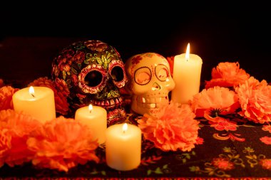 Siyah bir fonda iki zıt kafatası bulunur: biri metalik çiçeklerle süslenmiş, diğeri ise yanan bir mum tutmaktadır. Kadife çiçekleri ve mumlar Ölüm Günü 'nde şenlikli bir dokunuş ekler..