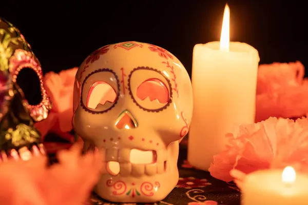 stock image A black backdrop features two contrasting skulls: one decorated with metallic flowers, the other holding a lit candle. Marigold flowers and candles add a festive touch on a Day of the Dead patterned cloth. decorated skull with metal flowers and a hol