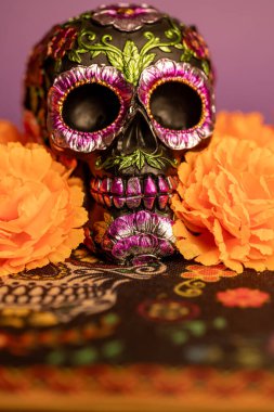 Parlak metal çiçeklerle süslenmiş ve parlak turuncu kadife çiçekleriyle çevrili bir kafatası. Dia de los Muertos 'u ve şenlikli ruhunu temsil etmek için ideal..