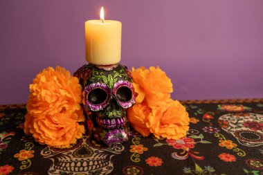 Metalik çiçeklerle süslenmiş ve üzerinde yanan bir mum olan bir kafatası. Turuncu çiçekler ve etrafındaki mumlar Dia de los Muertos 'u sembolize ediyor..