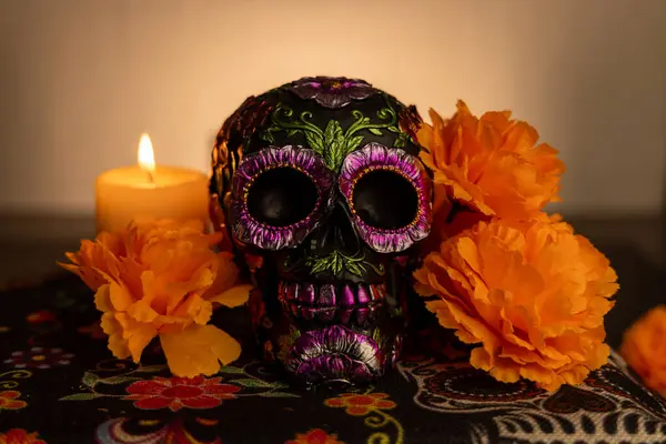 stock image Close-up of a skull decorated with metallic flowers, surrounded by bright orange marigold petals and an illuminated candle. The white gradient backdrop highlights this traditional Dia de los Muertos theme.