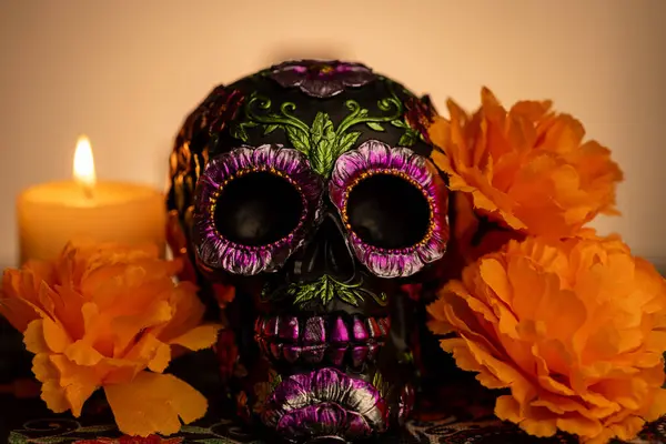 stock image Detailed view of a skull embellished with metallic flowers and encircled by bright orange marigolds. A nearby lit candle casts a soft light, reflecting the Mexican Day of the Dead festivities.