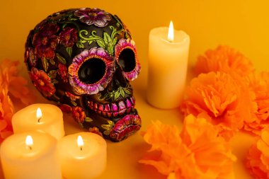 Kadife çiçekleri ve turuncu bir zemin üzerinde mumlar arasında dizilmiş metalik çiçekli siyah bir kafatası. Meksika 'dan Dia de los Muertos' a coşkulu bir saygı duruşu.