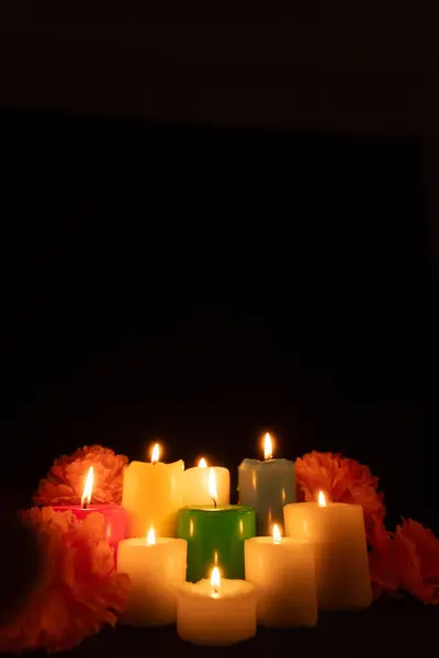 stock image A vertical shot of lit candles surrounded by marigold flowers, centered against a black background. The warm glow creates a serene atmosphere, perfect for Dia de los Muertos themes.