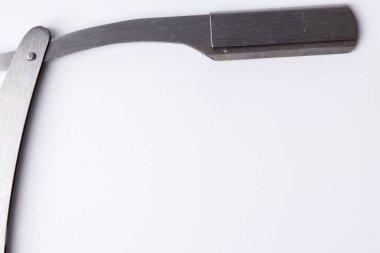 Açık bir berberin düz jiletini temiz beyaz bir arka planda detaylı bir şekilde görmek. Bıçak, görüntünün sol tarafında belirgin bir şekilde sergileniyor, ince işçiliğini tepeden tırnağa gösteriyor.