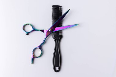 Görüntüye odaklanmış bir tarağın üzerinde duran bir makasın yakın çekimi. Temiz beyaz arkaplan araçları vurgular, onu kuaförlük veya tımarla ilgili içerik için ideal hale getirir.