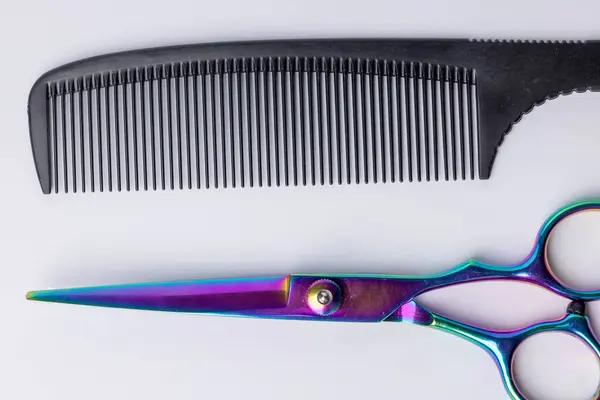 stock image A detailed top-down view of a black barber's comb and scissors centered on a white background. The clear focus on the tools highlights their professional quality